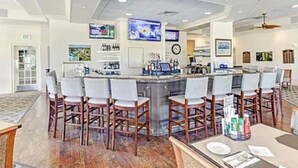 A bar area with a counter, bar stools, and a television screen. - Gated FoxFire Naples First-Floor/End-unit Amazing Water/Course View 27-Hole Golf (Naples)