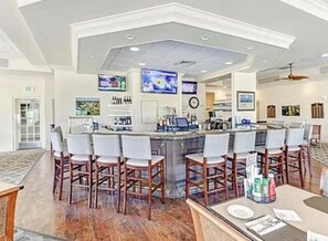 A bar area with a counter, bar stools, and a television screen. - Gated FoxFire Naples First-Floor/End-unit Amazing Water/Course View 27-Hole Golf (Naples)