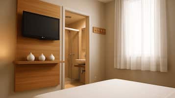 Una habitación de hotel moderna con una cama, un televisor montado, un estante de madera con jarrones, un baño con ducha y un ventanal con cortinas translúcidas.