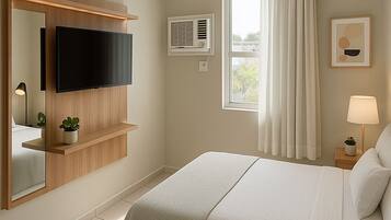 A hotel room with a large bed, a mounted TV, a window with curtains, a bedside lamp, and a small plant on the nightstand.