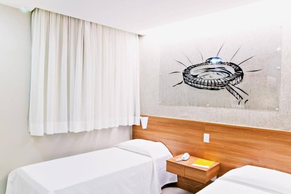 A hotel room with two beds, a wooden headboard, a nightstand with a phone and a yellow book, and a wall with a circular artwork.