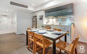 Una cocina moderna con horno empotrado, microondas y lavavajillas. Hay una mesa de comedor preparada para cuatro personas con sillas.