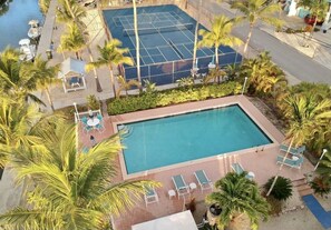 A pool area with a tennis court, lounge chairs, and palm trees.