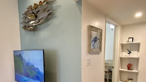 Ein Wohnzimmer mit einem Flachbildfernseher auf einem Holzständer, einer Wanddekoration und einem weißen Regal mit verschiedenen Gegenständen.