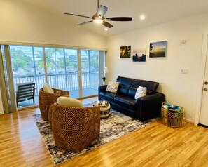 A spacious living room with a black leather sofa, wicker chairs, and a large window offering a view of the outdoors. - Beautiful Beach Home (Islamorada)