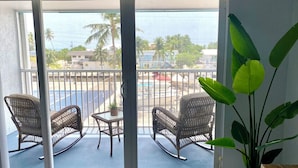 Ein Balkon mit Korbstühlen und einem kleinen Tisch, der auf eine Straße mit Gebäuden und Palmen blickt.