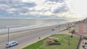 A coastal road with a beach view, a parking lot, and a building with a sign.