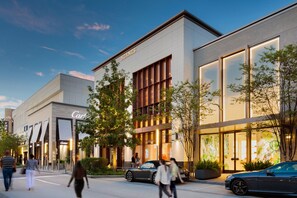 Ein modernes Gebäude mit einem markanten 'Hermes'-Schild, neben einem 'Carhartt'-Geschäft, das ein schlichtes architektonisches Design und einen gepflegten Außenbereich mit Bäumen und parkenden Autos aufweist.