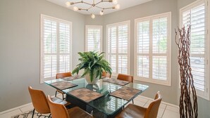 A dining room with a glass table, orange chairs, a potted plant, and a modern chandelier. - Stylish 3 Bedroom Sun City Grand Retreat w/ Resort Access in Surprise, Arizona (Surprise)