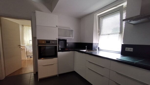 A modern kitchen with white cabinets, a black countertop, a built-in oven, and a window with blinds.