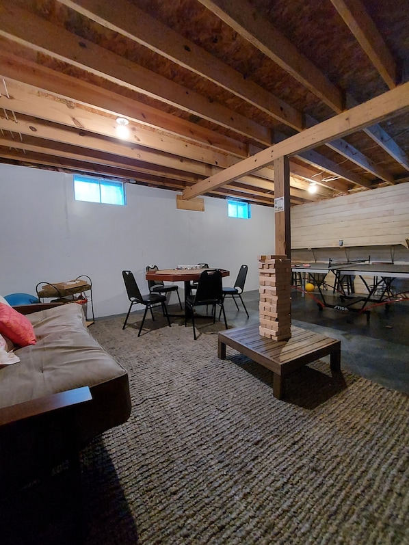 A cozy attic room with exposed wooden beams, a dining table with chairs, a sofa, and a small brick structure.