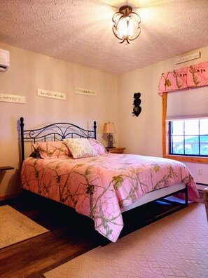 A bedroom with a bed, a nightstand, a lamp, a window with a view, and decorative wall art.