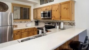Una cocina con armarios de madera, un refrigerador de acero inoxidable, un microondas y un lavamanos.