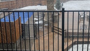 Un espacio exterior nevado con valla de madera, pared de piedra y barandilla de metal.