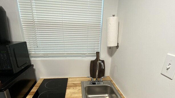 A compact kitchen with a black microwave, a wooden countertop, a stainless steel sink, and white cabinets.