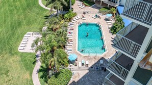 An aerial view of a hotel with a rectangular swimming pool surrounded by lounge chairs and umbrellas, a paved walkway, and a parking area. - BEAUTIFUL DIRECT GULF FRONT CONDO FORT MYERS BEACH 903B (Fort Myers Beach)