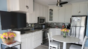 A modern kitchen with white cabinets, a stainless steel refrigerator, a microwave, and a dining area with a table and chairs. - BEAUTIFUL DIRECT GULF FRONT CONDO FORT MYERS BEACH 903B (Fort Myers Beach)