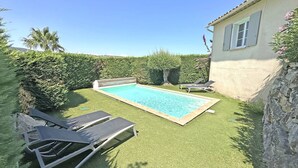 A rectangular swimming pool with a tiled edge, surrounded by artificial grass. There are two lounge chairs and a small shed in the background.