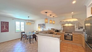 A modern kitchen with a central island, a dining area with chairs, and a large window providing natural light.