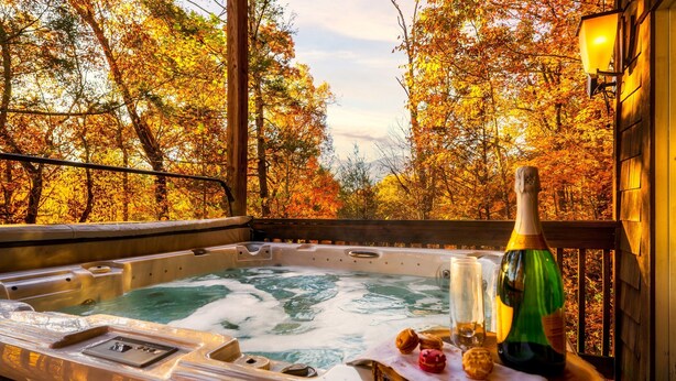 Een hottub met een houten terras, omringd door herfstbladeren.