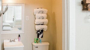 Une salle de bain avec un lavabo blanc, des toilettes et un miroir au-dessus. On y trouve des articles de toilette sur le lavabo et le sol est en bois.