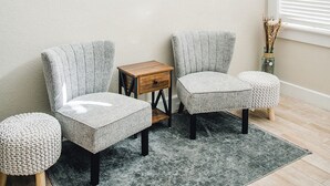 Une pièce comprenant deux fauteuils, une petite table d’appoint en bois et un tapis gris posé sur un plancher en bois.