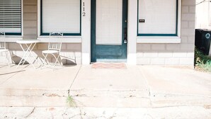 Un bâtiment avec une porte à volets fermés, un numéro de maison bien visible et un petit espace extérieur aménagé avec des chaises.