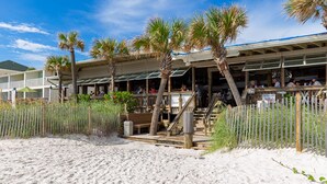 Ett hotell vid stranden med uteservering, palmer och en sandstrand.