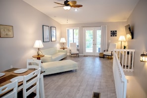 A spacious living area with a sofa, chairs, a dining table, and a ceiling fan.