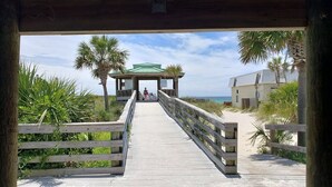 En träpromenad som leder till en överbyggd paviljong med utsikt över stranden och havet.