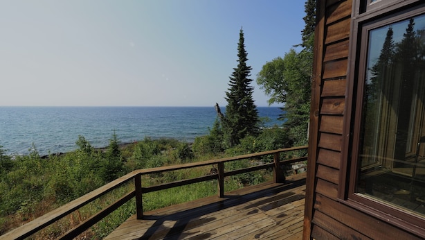 A wooden deck with a railing overlooking a body of water and greenery. - Off-Grid On Superior: Entire Private Cabin On Lake Superior (Hovland)