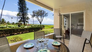 A round table with plates and glasses, a chair, and a view of a landscaped garden and ocean.