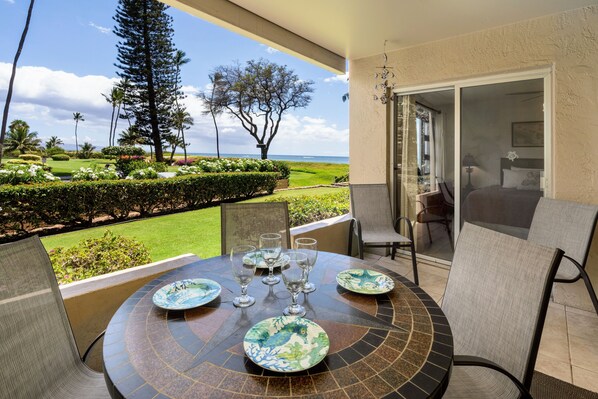 Une table ronde avec des assiettes et des verres, une chaise, et une vue sur un jardin aménagé et l’océan.