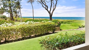 A well-maintained garden with a lawn, various shrubs, and trees, leading to a view of the ocean.
