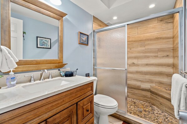Un baño con tocador de madera, un espejo grande, un lavabo blanco y una ducha con pared de madera.