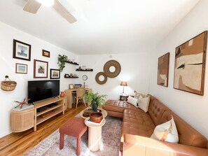 A living room with a flat-screen TV, a brown leather sofa, a wooden coffee table, and a red bench.