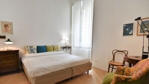 A bedroom with a bed, a chair, a desk, a lamp, and a window.