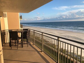 Een balkon met een tafel en stoelen, met uitzicht op het strand.