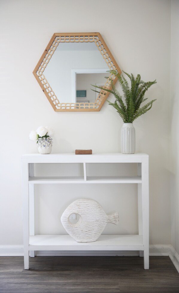 A white console table with a mirror, a vase with green plants, and a decorative fish-shaped object.
