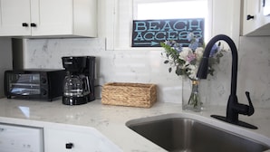 Una cucina con mobili bianchi, un tostapane, una macchina da caffè, un lavello e un cartello con la scritta 'BEACH ACCESS'.
