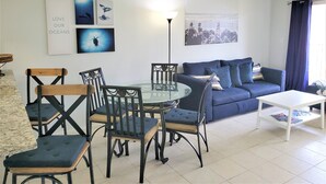 Un salon avec une table à manger en verre, des chaises recouvertes d’un tissu bleu, un canapé bleu et une table basse blanche. On y trouve également des œuvres d’art murales et un lampadaire.