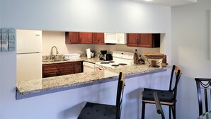 Une cuisine dotée de plans de travail en granit, de meubles en bois, d’un four à micro-ondes, d’une cuisinière et de deux tabourets de bar.