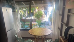 Una cocina pequeña con un refrigerador, una mesa de comedor con sillas y vistas a un jardín a través de una ventana.