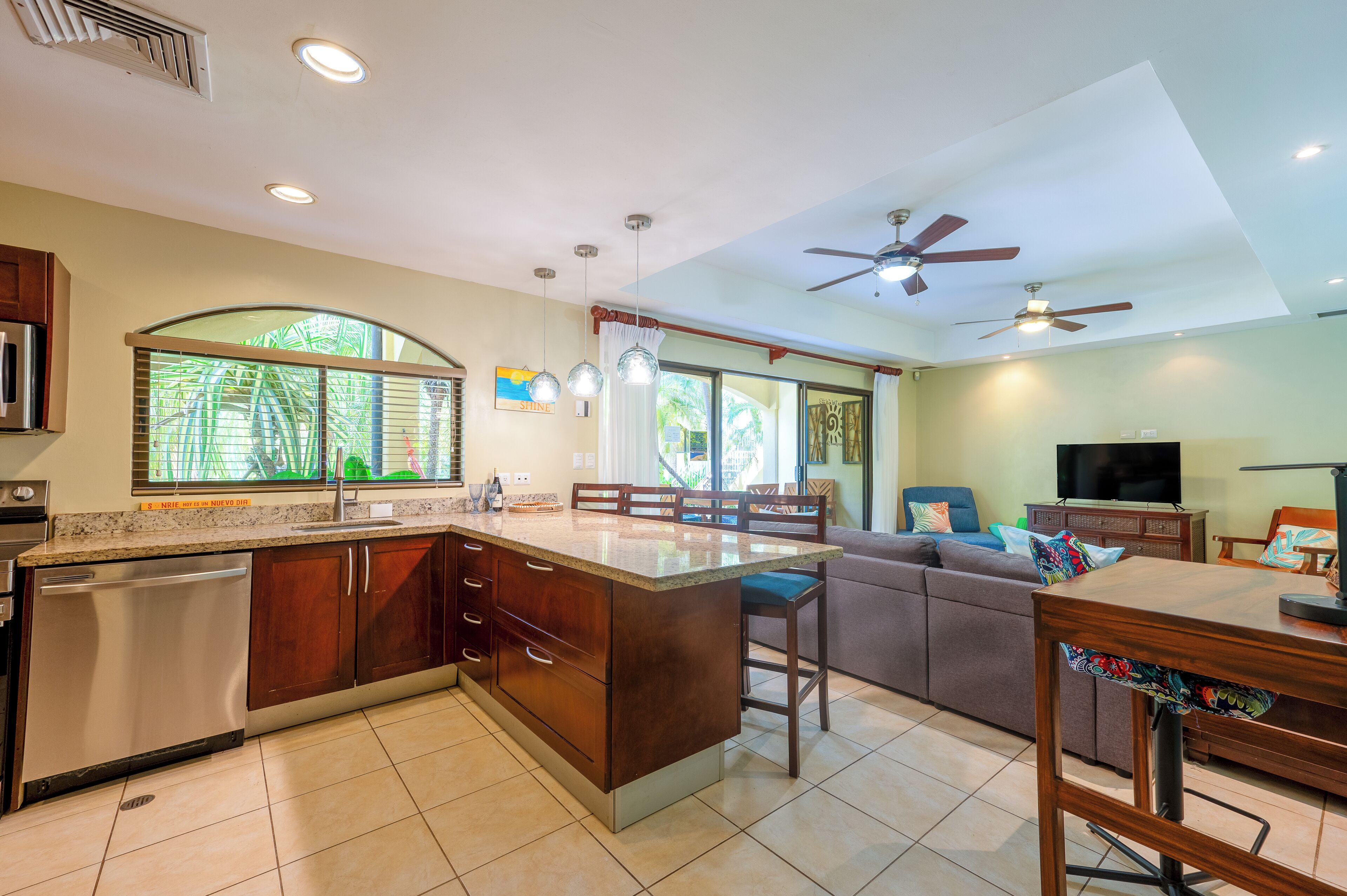 A spacious kitchen with a central island, a dining area with a table and chairs, a living room with a sofa, and a ceiling fan.