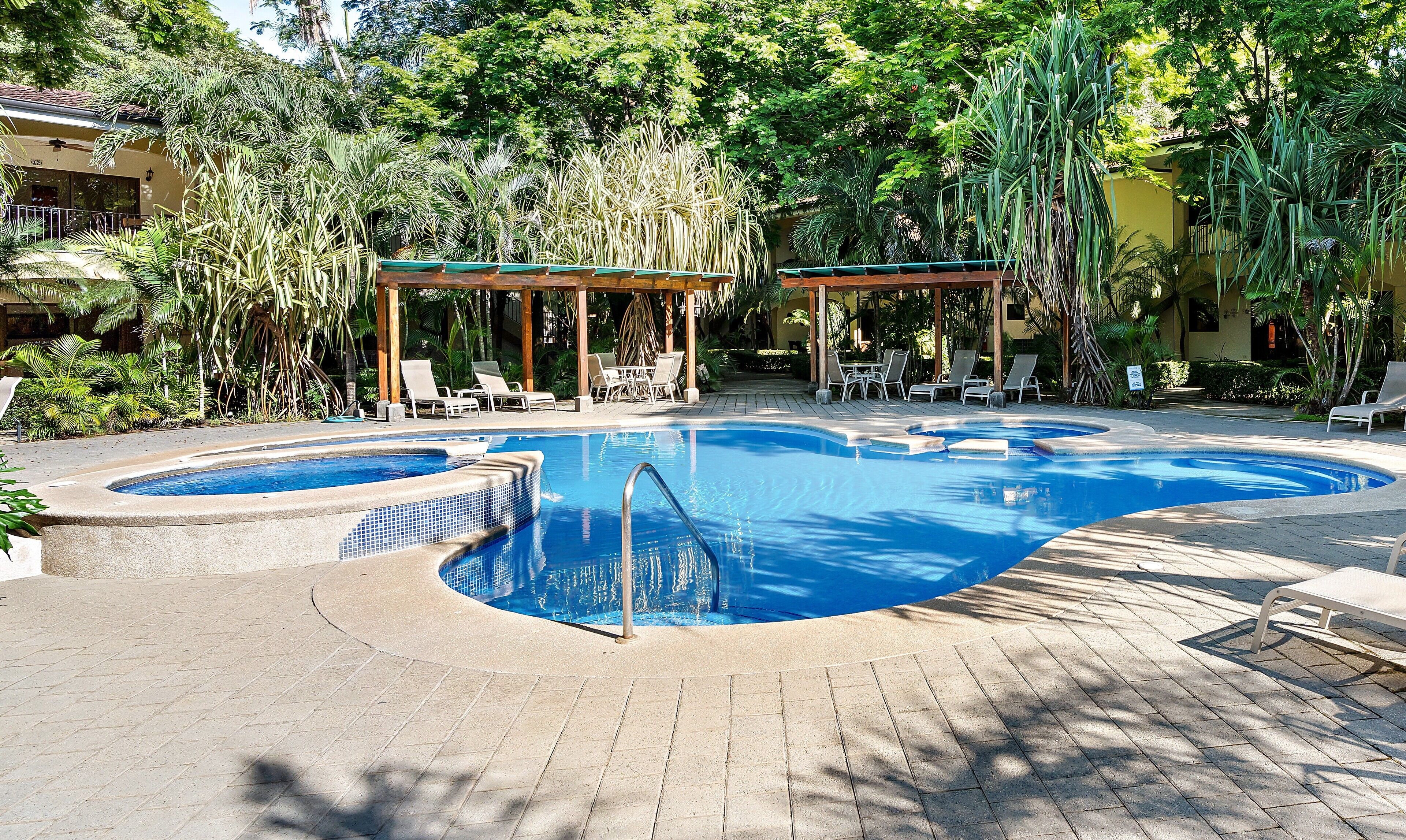 A pool with a curved design, surrounded by lounge chairs and a covered seating area.