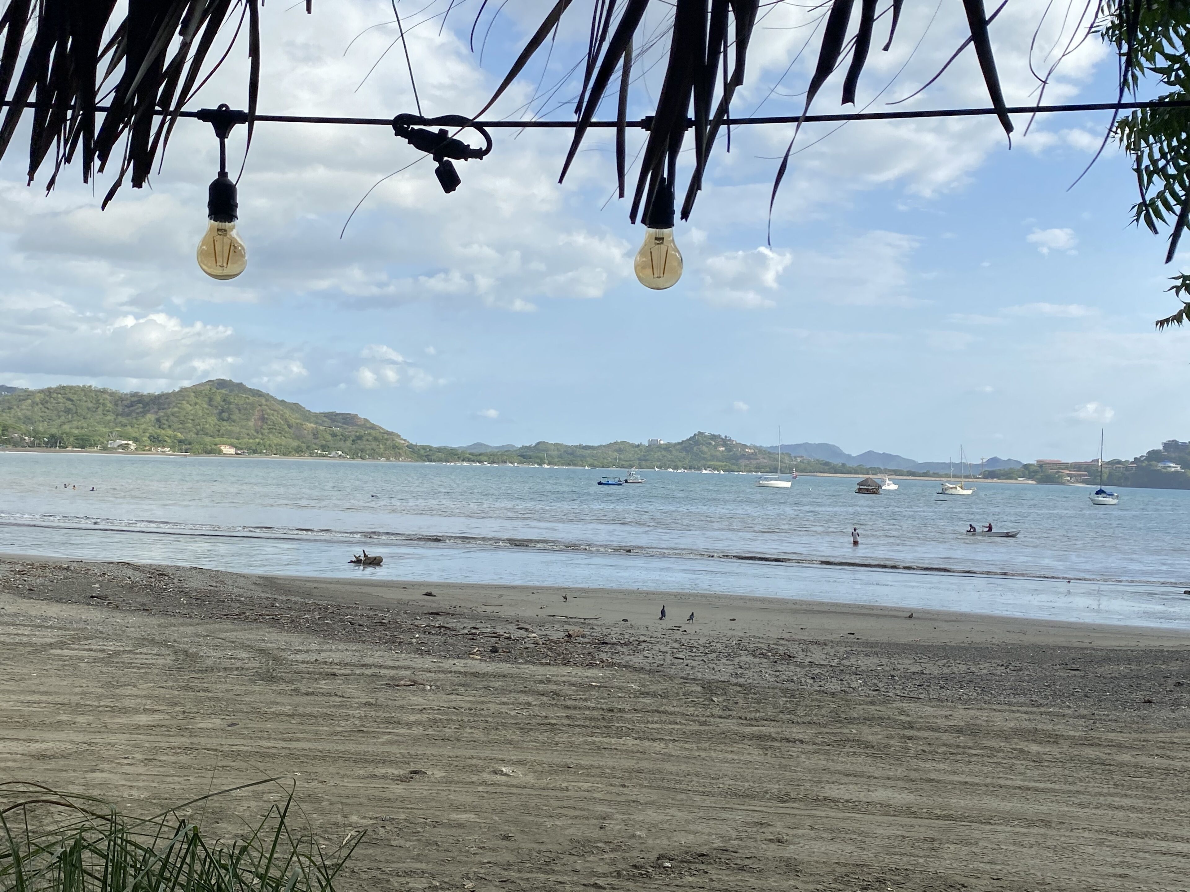 Une plage offrant une vue dégagée sur la mer, les bateaux et les collines lointaines.