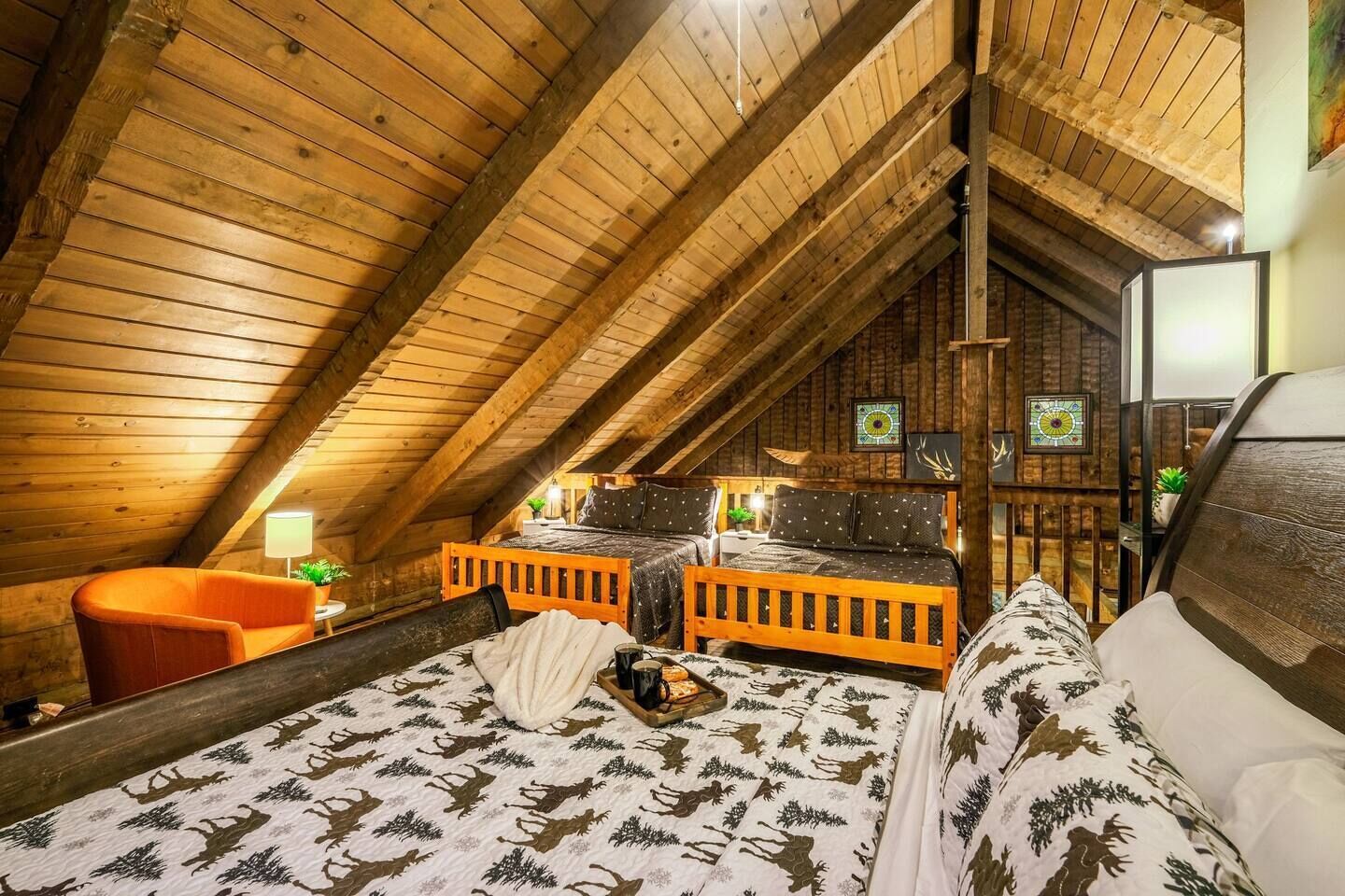 Ein gemütliches Schlafzimmer im Dachgeschoss mit Holzbalken, einem Bett mit gemusterten Textilien, einem Sessel und einem kleinen Tisch mit Lampe.