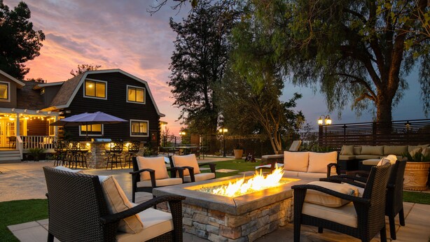 A patio with wicker furniture and a stone fire pit. - Chateau Syrah by AvantStay | Picturesque Estate w/ Pool, Pickleball, Hot Tub (Temecula)