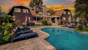 A two-story log cabin with a swimming pool, outdoor seating, and a stone chimney. - Chateau Syrah by AvantStay | Picturesque Estate w/ Pool, Pickleball, Hot Tub (Temecula)