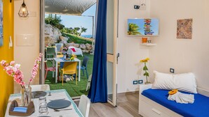 A room with a bed, a dining table with chairs, a TV, and a view of the outdoors. - Apt Perterrepermari a 2 Km Da Riserva Dello Zingaro (Castellammare del Golfo)